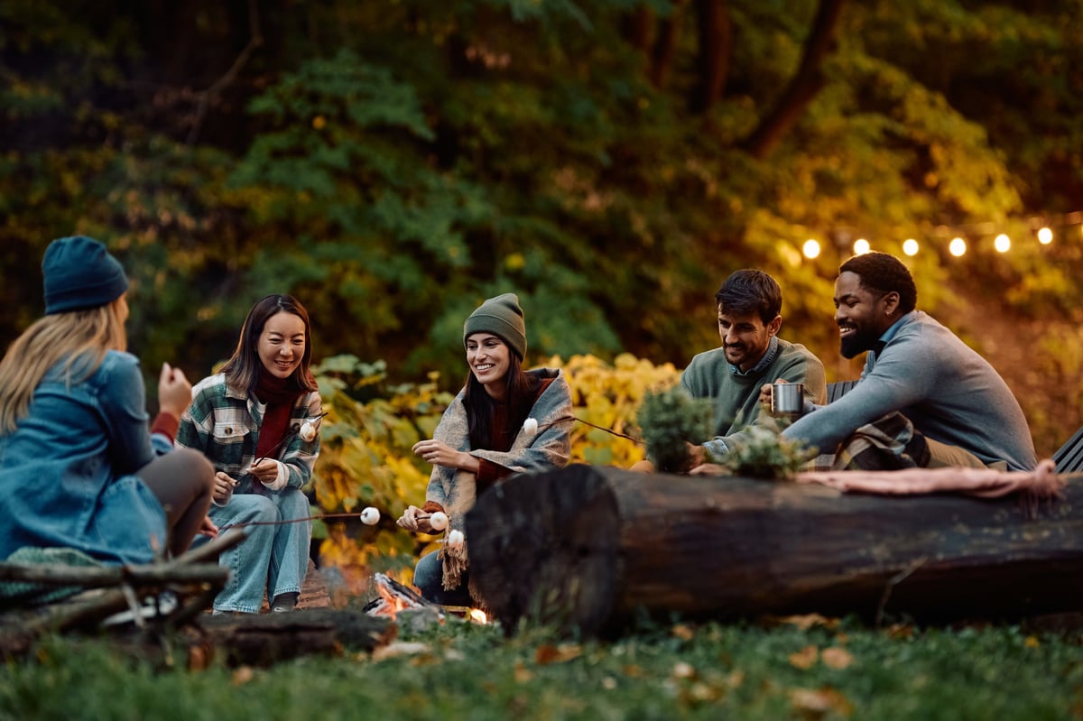 Grupo de amigos asando malvaviscos junto a la fogata en un campamento de otoño