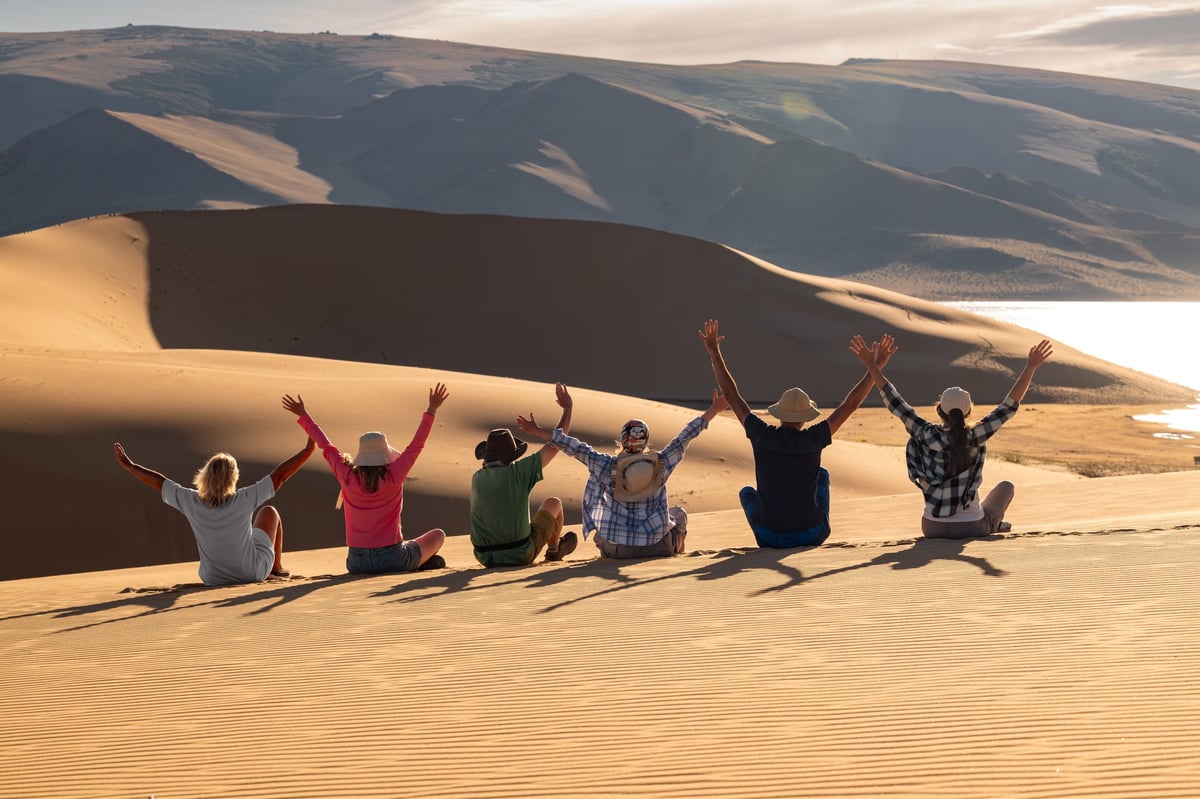 Grupo de viajeros con los brazos abiertos en una duna del desierto junto al mar