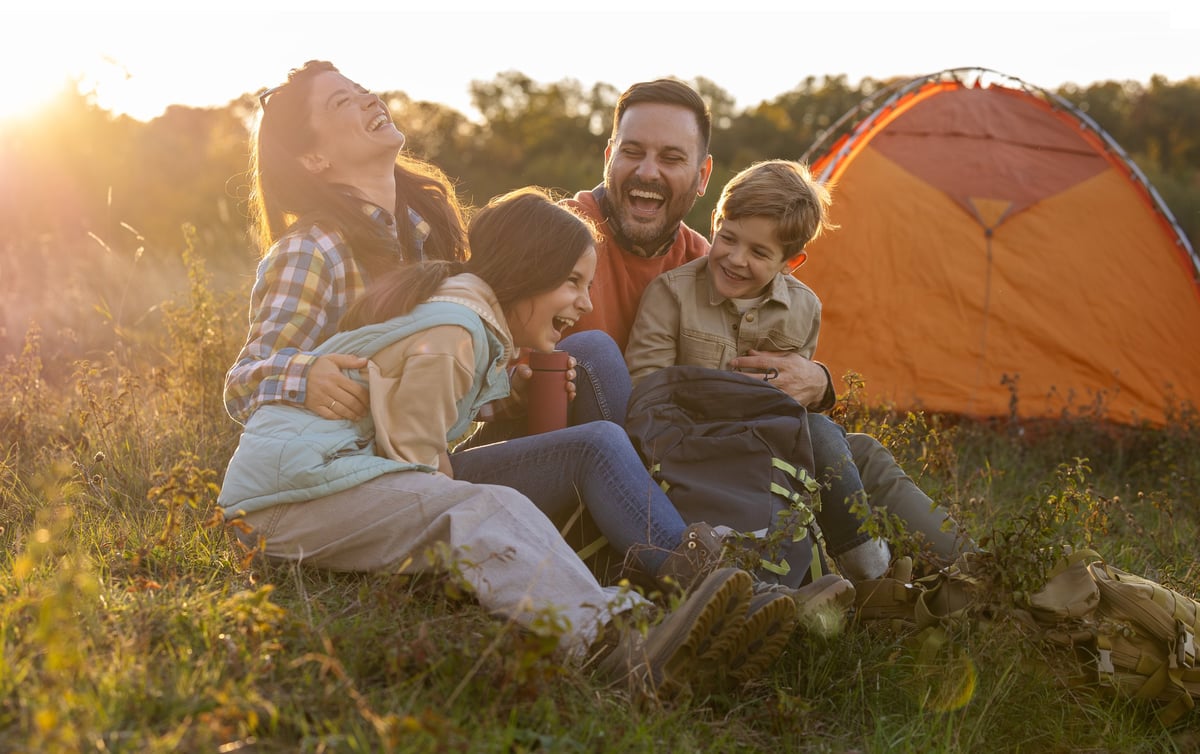 Familia compartiendo una fogata junto a su casa de campaña al atardecer